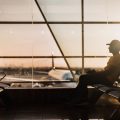 man sitting an an airport against glass panelled window with planes in the background