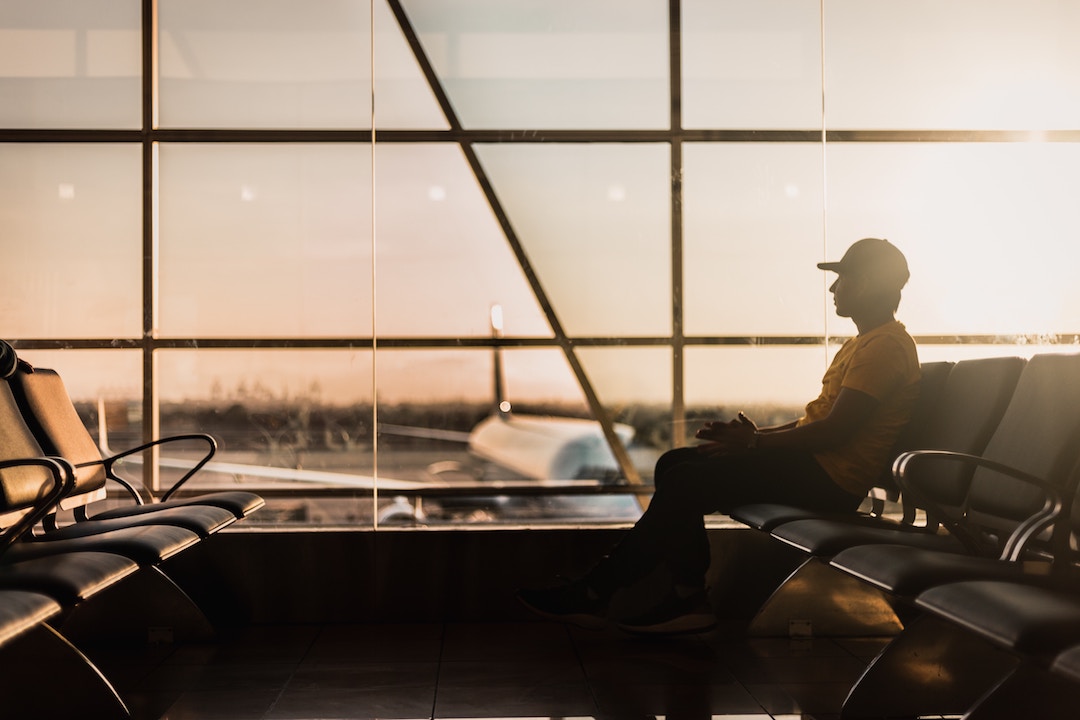 man sitting an an airport against glass panelled window with planes in the background