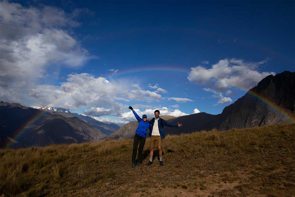 two people in the mountain waving at the camera