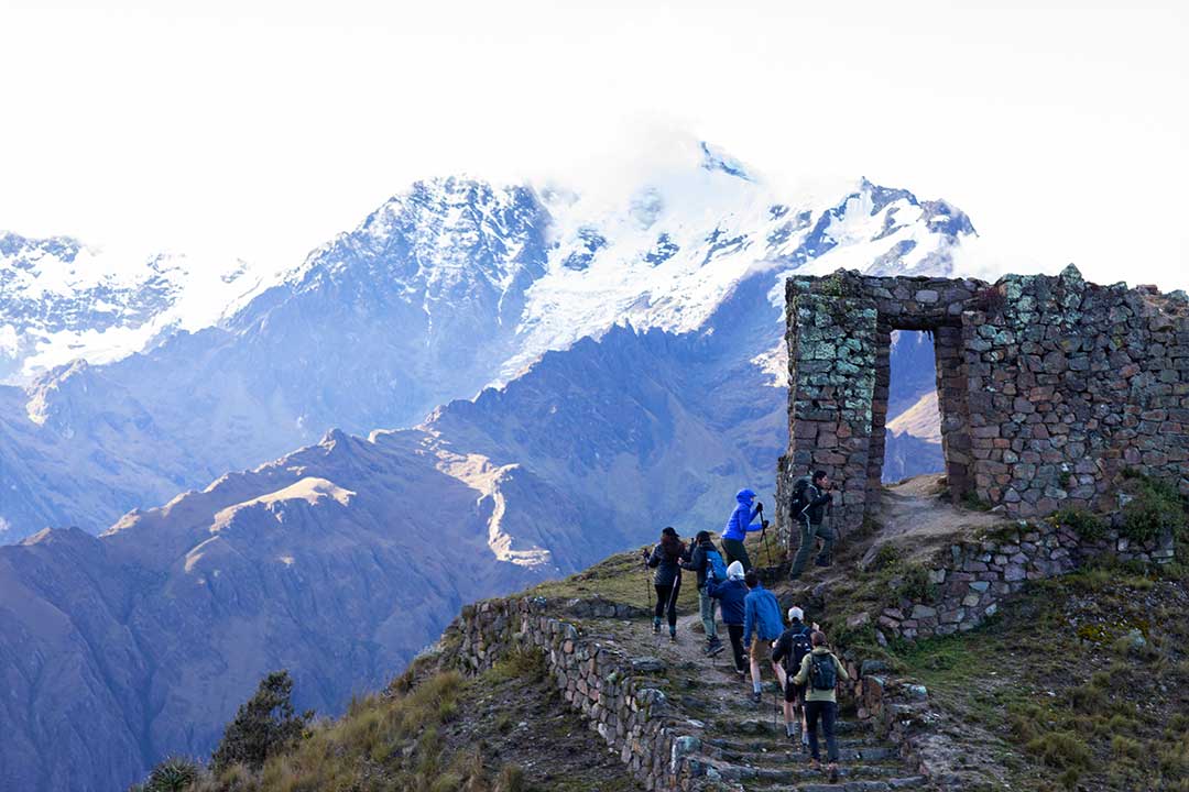 a group of trekkers walking up to a stone doorway structure in the mountains