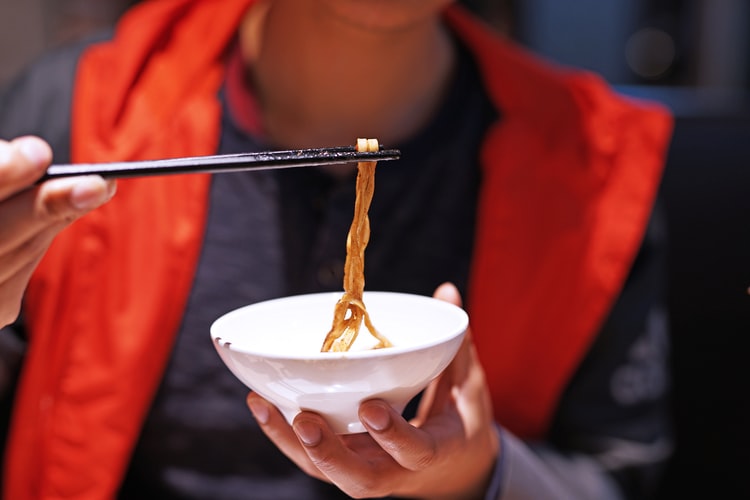 close-up photography of man using chopsticks on noodles