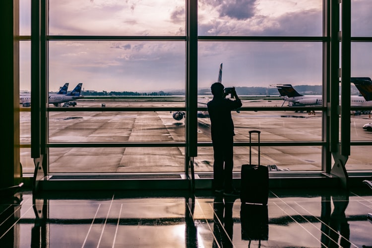 a man standing in an airport taking pictures through the window of planes landing