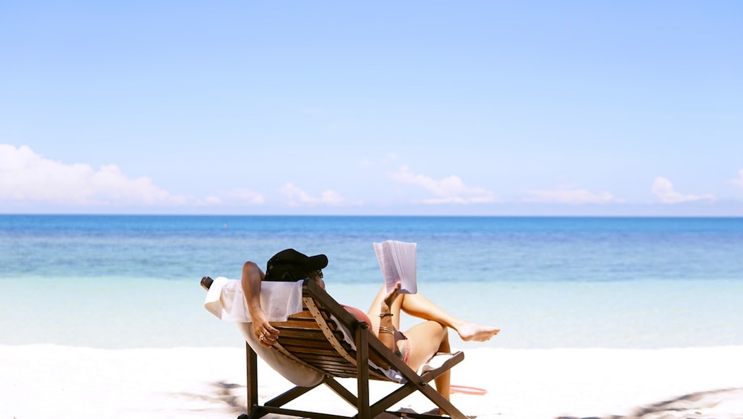 woman sits on brown wooden beach chair in front of the sea