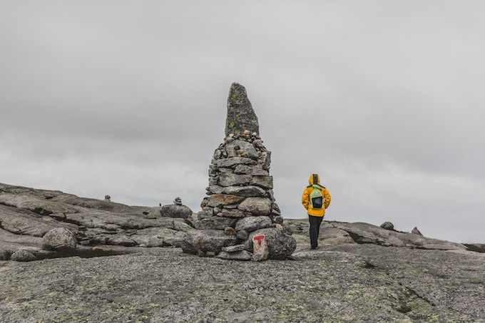 A woman in a yellow coat posing by a rock formation in Kjerag, Norway