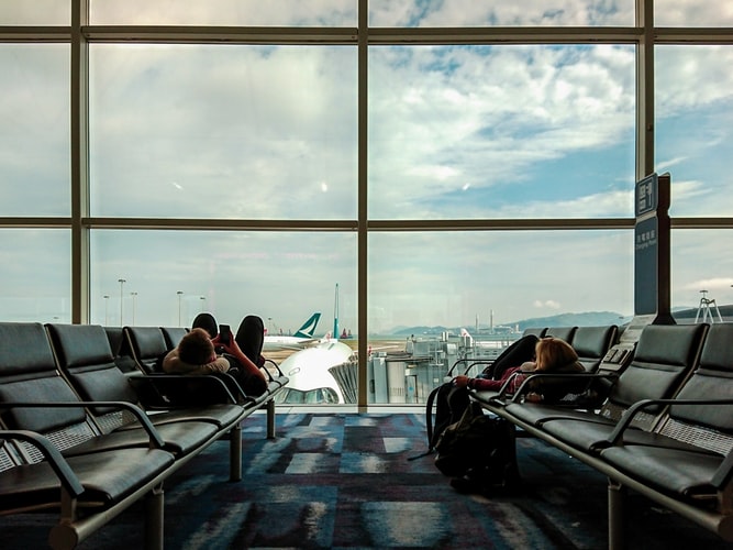 two people lying on seats in an airport in front of the window