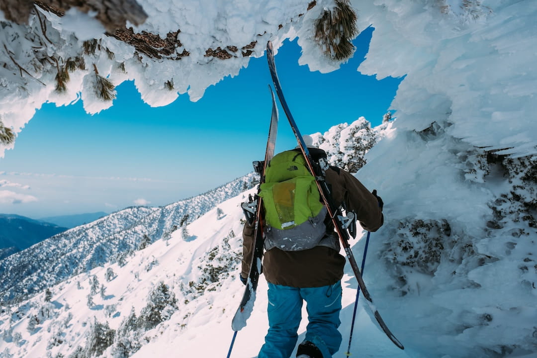 A man wearing a green backpack carrying skis walking through an ice tunnel