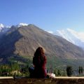 a girl sitting on a wall overlooking a mountain