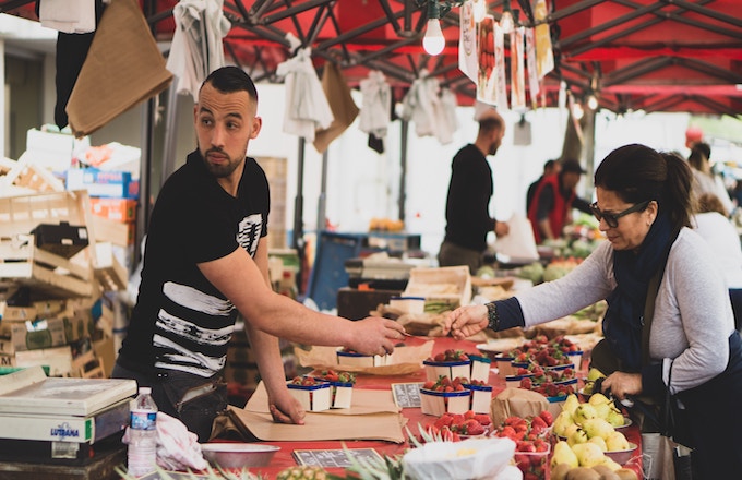 A man selling a basket of strawberries to a woman