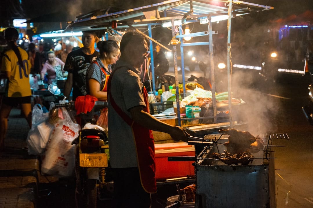 A man roasting chicken at a market in Laos