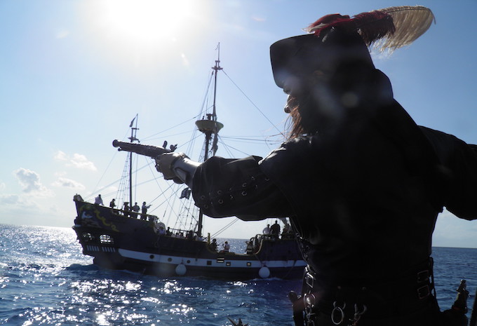 A man dressed as a pirate pointing a gun at a pirate ship