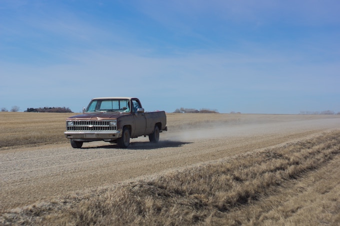 A vintage pick up truck driving down a dirt road in Saskatchewan, Canada