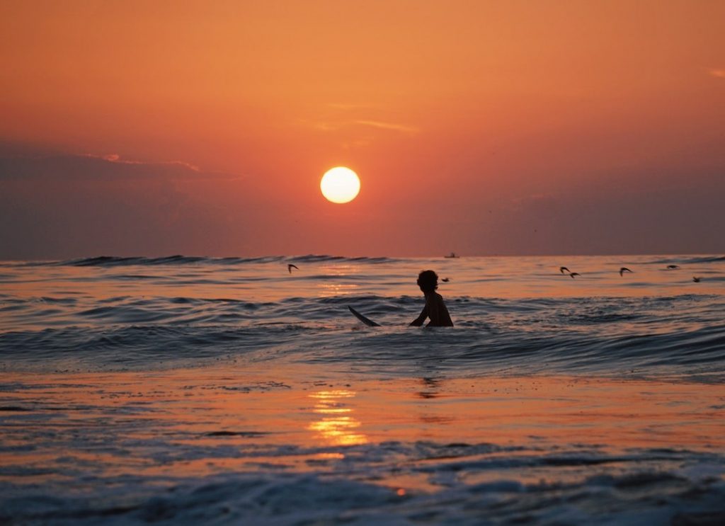 Person floating in the surf at sunset