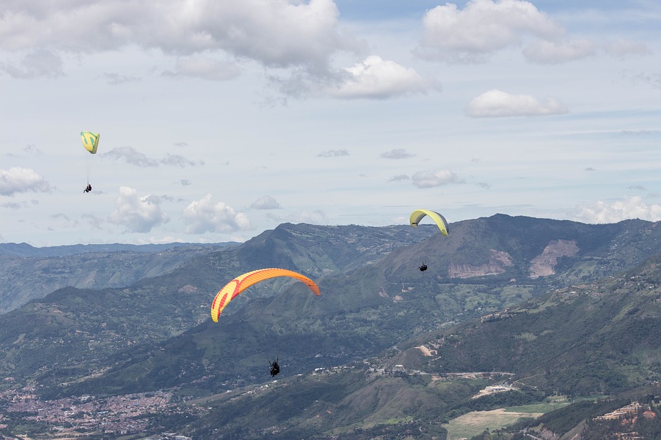 three paragliders soaring through the air across a mountain range