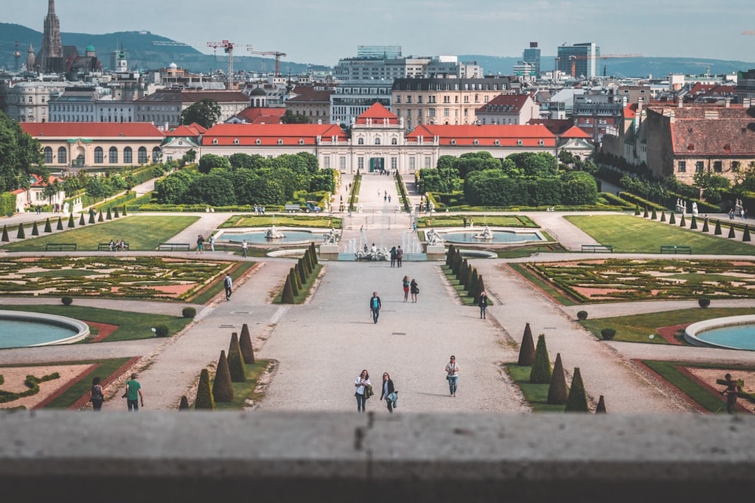 group of people walking on park with a beautiful building in the background and manicured gardens