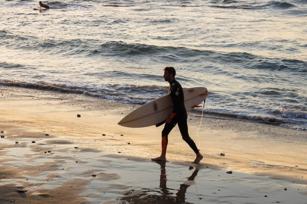 Man holding a surfboarding walking toward the beach in Tel Aviv, Israel