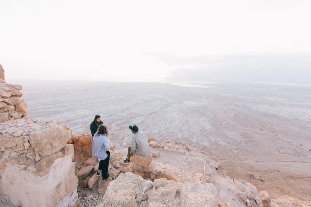 Three people standing on the edge of a cliff in Masada National Park, Israel