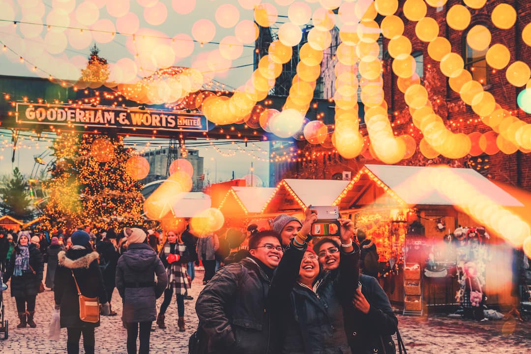 People taking a group photo beneath twinkling lights at the Toronto Christmas Market