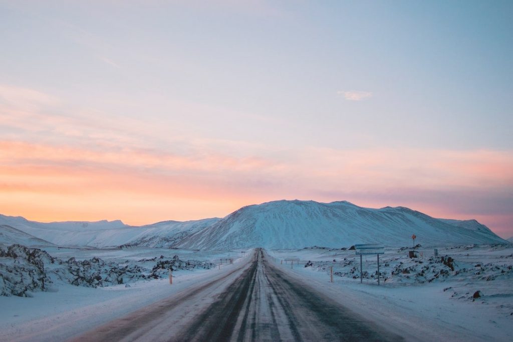 An empty road dusted in snow with a mountain in the background in Iceland