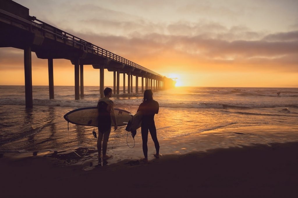 Two people standing on a beach holding surfboards at sunset