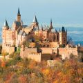 a castle on top of a hillside covered in trees with autumn colours of red, orange and brown