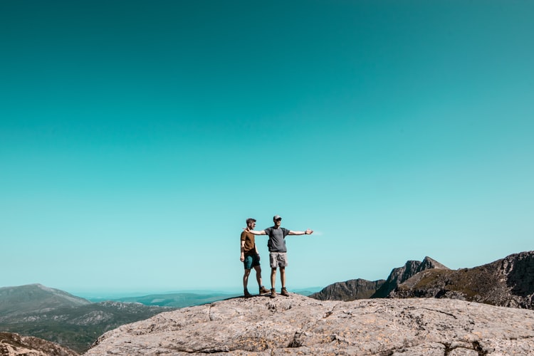 two men standing on top of grey rock hill