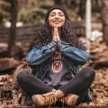 a girl smiling as she sits crosslegged and meditates with her hands in prayer