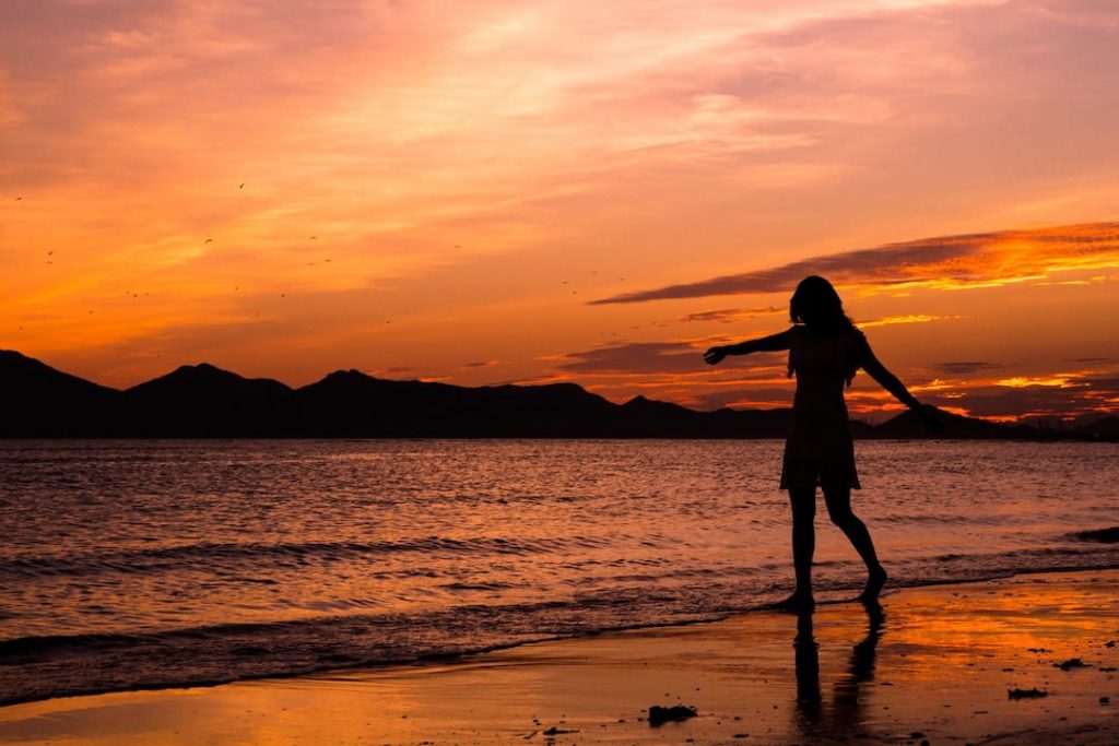 Silhouette of a woman at the shoreline of a beach at sunset