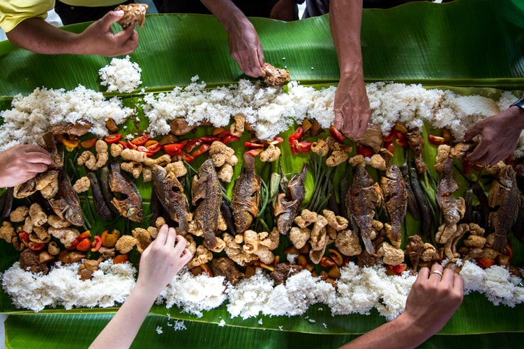 a banana leaf covered in rice and fish with lots of hands eating it 