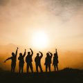 Silhouette of a group of people giving the peace sign in front of a sunset