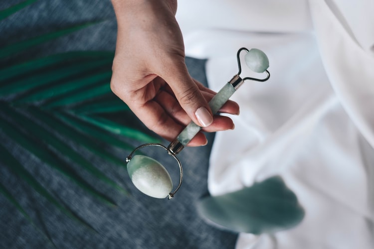 a green jade facial roller being held in a hand