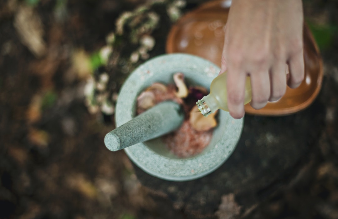 Person pouring oil into a mortar and pestle filled with rose petals