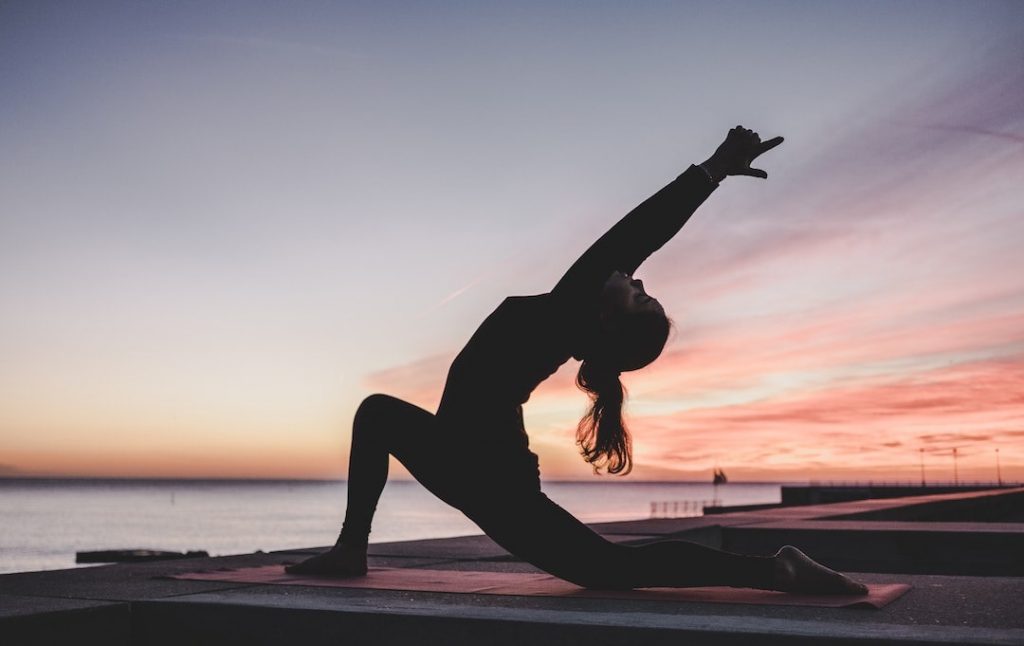 Woman on a dock at sunset doing yoga