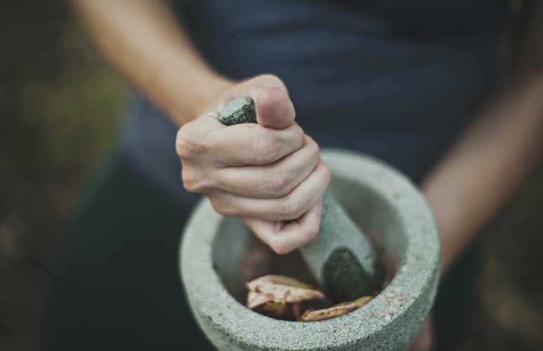 a woman crushes rose petals and other ingredients in a stone bowl