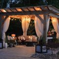 Outdoor furniture inside a gazebo with drapes and string lights