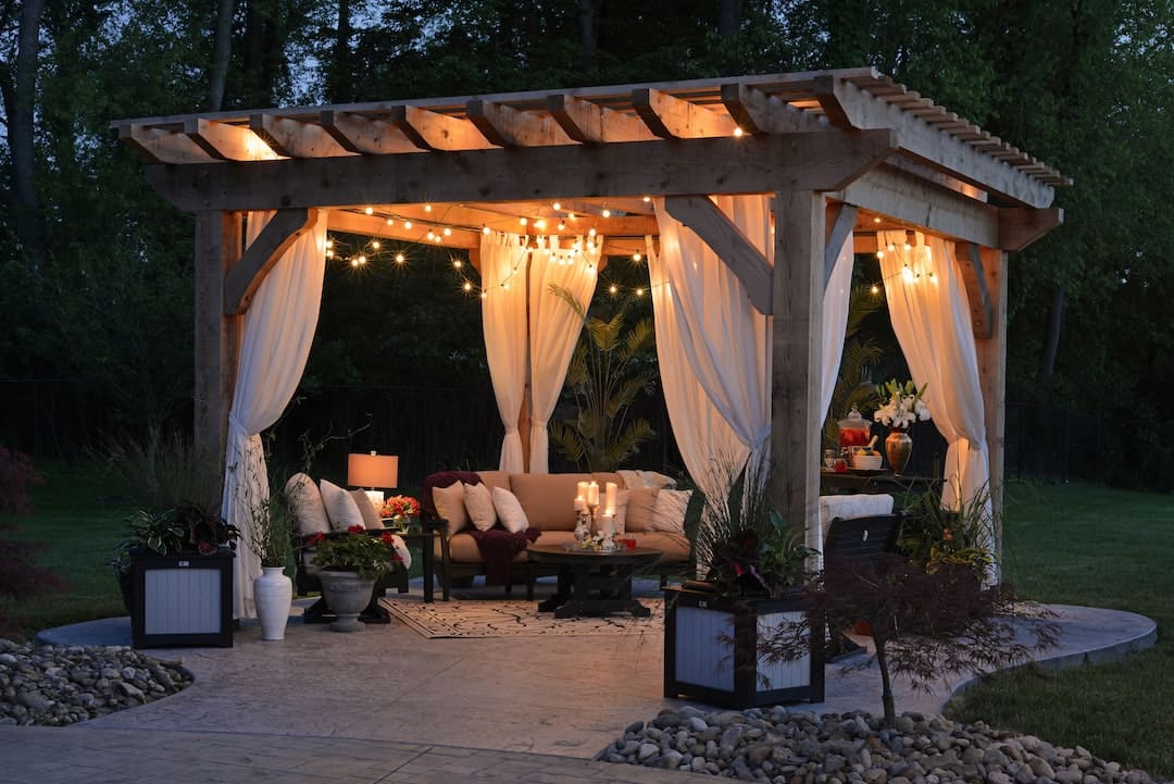 Outdoor furniture inside a gazebo with drapes and string lights