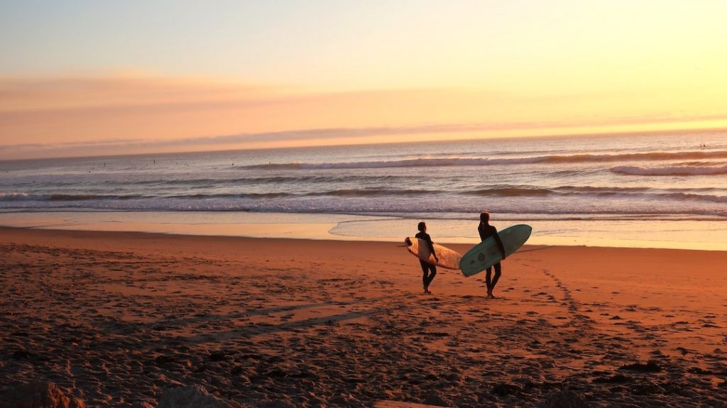 Two people walking on a beach holding surfboards