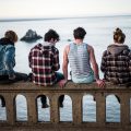 Four people sitting on a railing overlooking the sea