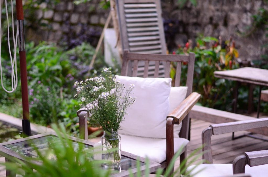 Wooden chair with white cushions beside a vase of flowers in a yard