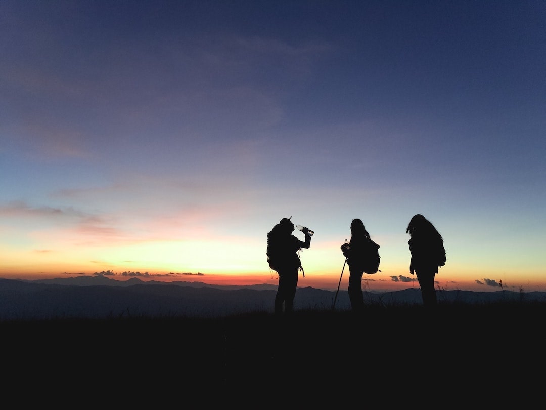 Three people with backpacks standing on a mountain at sunset