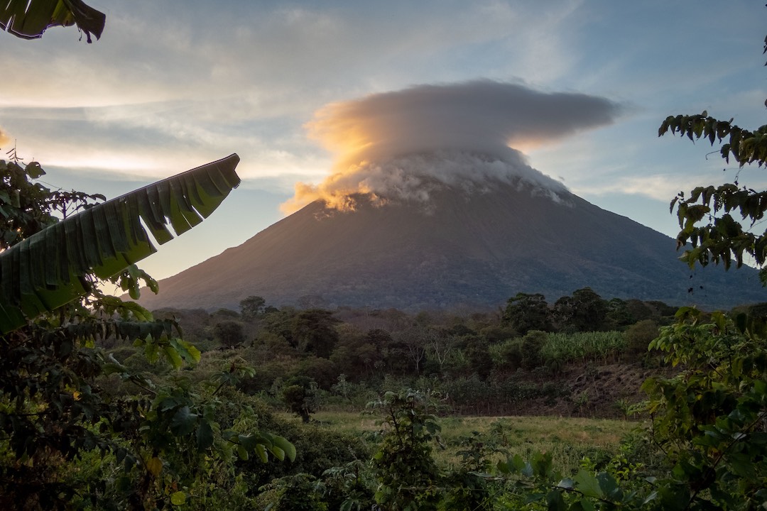 a volcano surrounded by greenery and a cloud