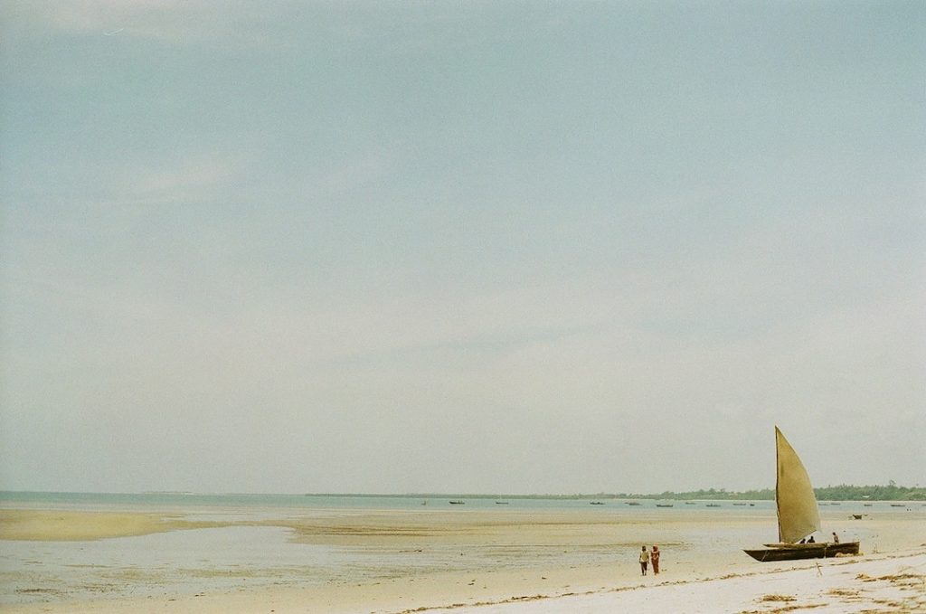 People walking on a beach beside a sailboat in East Africa