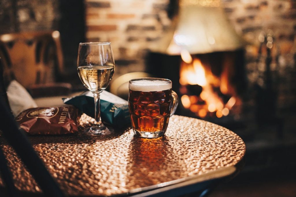 Glass of wine and mug of beer on table with a fireplace in the background