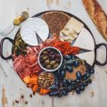 Cheese board with meat, olives, grapes, and a baguette