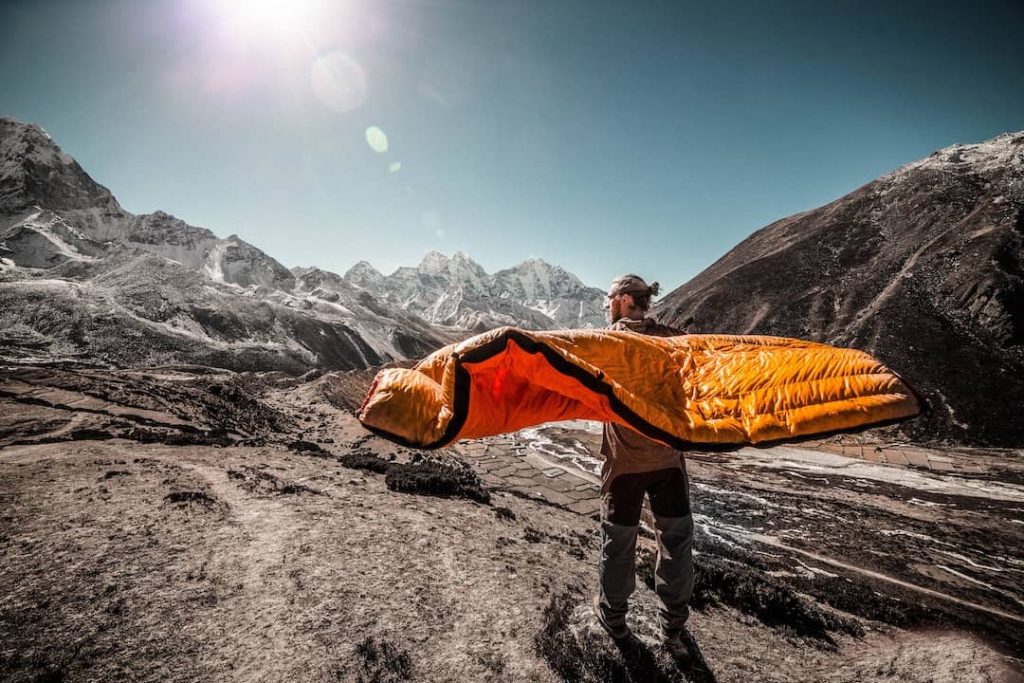 Man standing on trail holding orange sleeping bag at Everest Base Camp