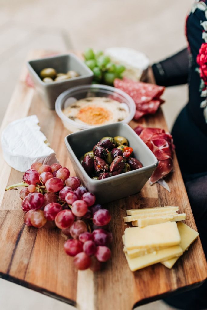 Person holding cheese platter with grapes and olives