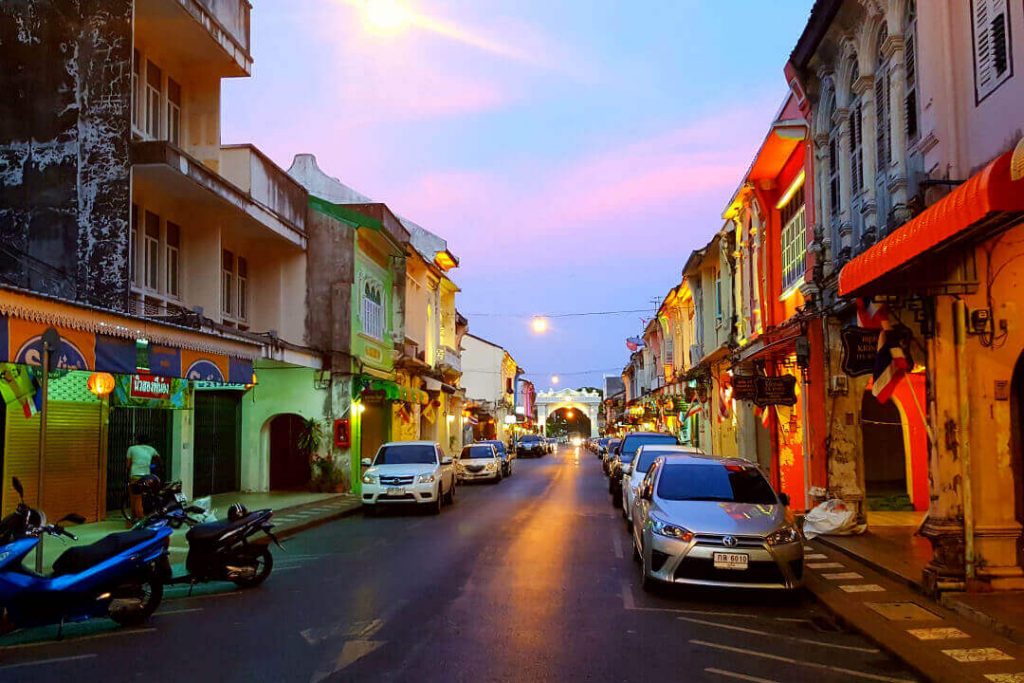 A night time view of the Old Town Phuket, Thailand street with cars parked on either side and lights casting a nice yellow glow.