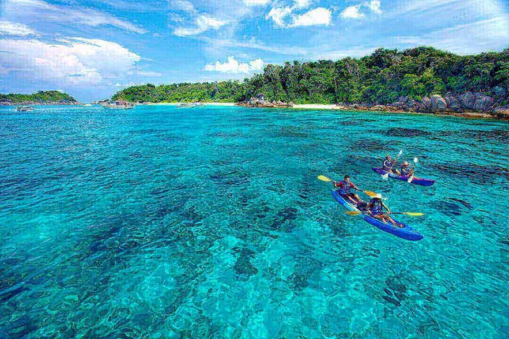 Two kayaks, each with two people in them, explore the beautiful blue waters of the Similan Islands, Thailand. 