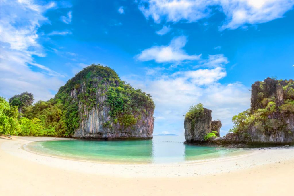 A beautiful image of a Phuket, Thailand beach with no one around but the limestone rocks, emerald water, and golden sandy beach. 