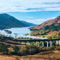 View over Glenfinnan valley with steam train on viaduct and Loch Shiel in the background, Highlands, Scotland.