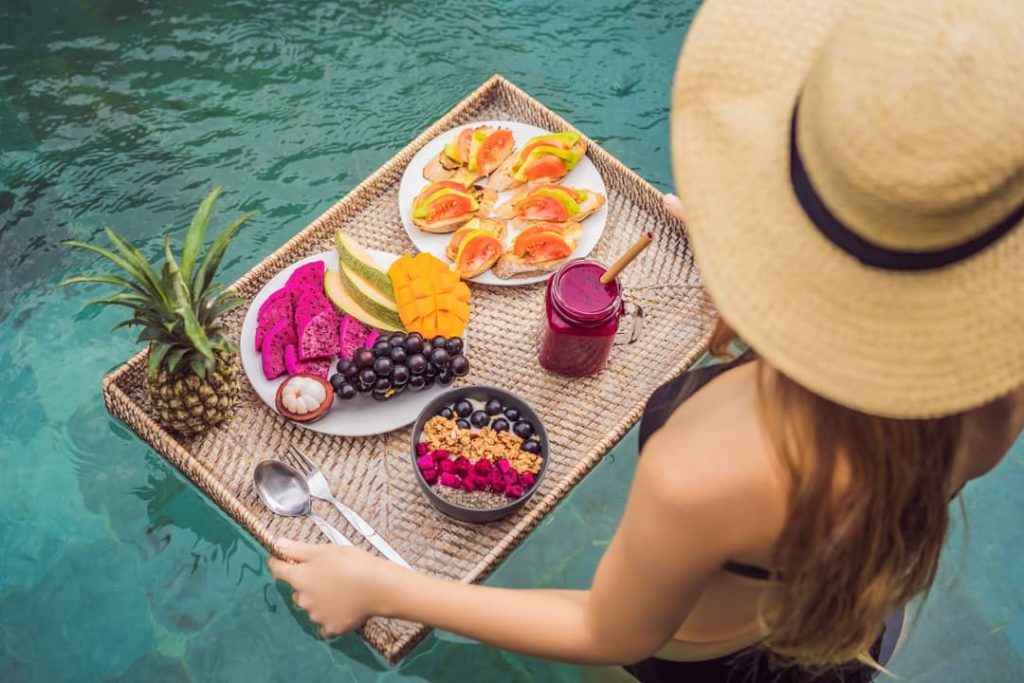 A young woman improves her well-being by enjoying a floating fruit platter in the swimming pool of a luxury hotel.